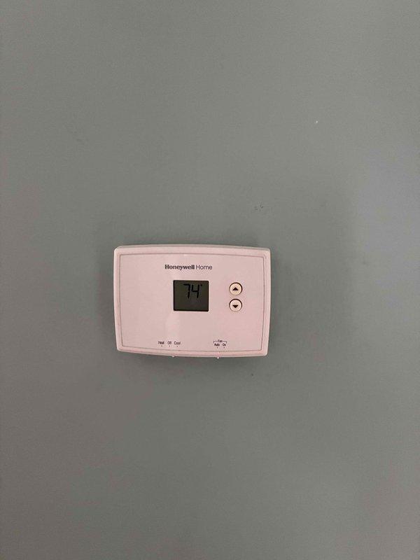 Conducted comprehensive estimate for replacement of existing 10-12 ton air conditioning system with outdoor condensing unit and gas heating equipment, currently operational. Documented existing Honeywell Home thermostat with digital display reading 74 degrees, featuring standard heat/cool selector and fan control with auto/on positions for replacement system specifications.