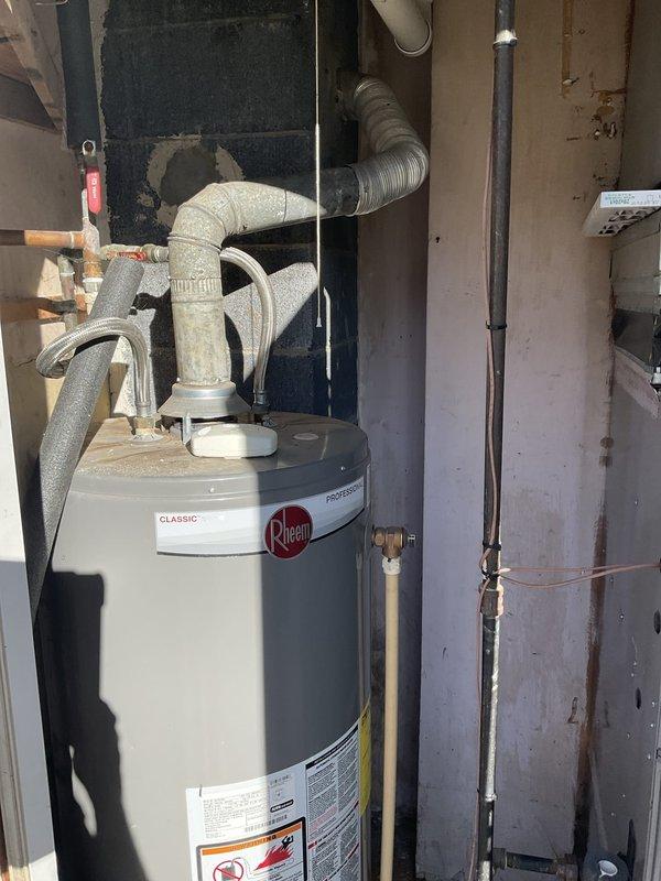 Conducted comprehensive site assessment for HVAC system replacement in residential basement utility area. Evaluated existing furnace and air handler configuration, documenting current installation including PVC venting system with multiple 90-degree bends, copper refrigerant lines, and electrical connections. Photographed complete system setup showing gray metal furnace unit with mounted air handler above, noting black coupling bands at pipe connections and red-handled valve positioning. Assessed Rheem Classic water heater in adjacent mechanical space, examining flexible ductwork connections, silver and white ribbed ducting secured with metal clamps for exhaust and intake systems. Documented copper piping connections at water heater base and reviewed overall mechanical infrastructure within exposed framing environment. Prepared detailed photographic documentation of all components for replacement estimate preparation.