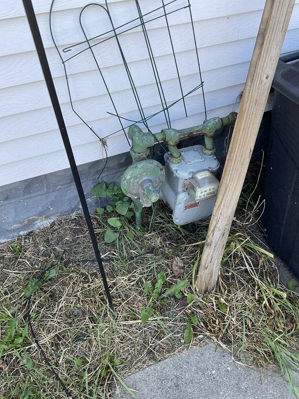 Completed on-site evaluation of existing residential air conditioning system for replacement estimate. Documented current outdoor condensing unit condition, noting aging equipment with weathered components, overgrown vegetation around unit base, and installation on concrete pad adjacent to building foundation. Photographed unit placement, electrical connections, and surrounding area to assess accessibility for future replacement work and identify any potential installation considerations.
