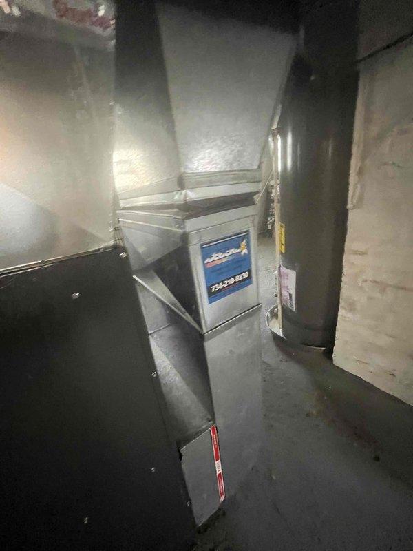 # HVAC Service Report - No Cool Condition

Responded to service call for air conditioning system not producing cold air on aging residential HVAC unit. Upon arrival, conducted visual inspection of basement-installed furnace and air handler assembly. System appeared to be 10+ years old based on equipment condition and manufacturer specifications visible on unit labeling.

Performed diagnostic evaluation of cooling system components. Assessed ductwork connections, including vertical black metal supply duct and horizontal distribution runs extending from furnace unit. Verified proper airflow through system and checked for obvious mechanical failures or disconnections in ductwork assembly.

Documented existing equipment configuration showing gray metal furnace unit with attached air handling components and associated ventilation infrastructure. Captured photographic evidence of installation setup, including manufacturer identification plate and warning labels for service records.

Based on