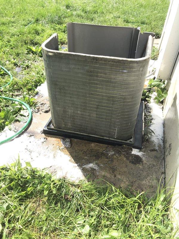 Responded to no-cool service call on 10+ year old outdoor condenser unit located behind residence with reported non-spinning blades. Upon arrival, removed top panel and performed visual inspection of internal components including condenser coil, compressor, and refrigerant lines. Inspected fan motor assembly and blade mechanism to diagnose failure cause. Photographed unit condition showing condenser coil, compressor with copper line connections, and overall equipment installation on concrete pad. Unit assessed for operational status and component functionality to determine necessary repairs for restoring cooling operation.