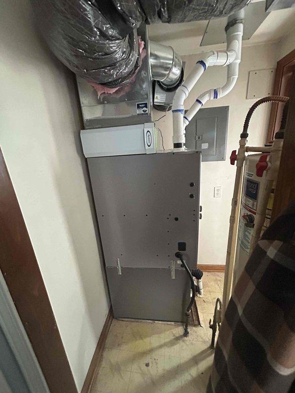 Completed installation of 3-ton air conditioning system with matching evaporator coil in residential utility room. Unit positioned on right side with proper clearances, all refrigerant lines connected, condensate drainage routed through PVC piping system, and electrical connections made to existing breaker panel. System tested and operational upon completion.