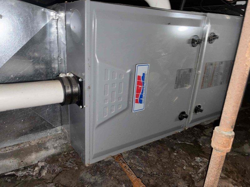 Conducted comprehensive assessment of non-operational air conditioning system with aging 2-ton to 4-ton capacity unit. Inspected air handler unit located in crawl space, evaluating overall condition of equipment including cabinet integrity, access panel security, and surrounding installation environment. Documented existing PVC condensate drainage system with proper trap configuration and mounting hardware. Photographed current equipment setup showing air handler mounted on concrete pad with metallic supply ductwork connections and white PVC drain line secured with appropriate clamps. Assessed crawl space conditions including clearances, floor surface, and accessibility for replacement work. Provided customer with detailed estimate for complete system replacement due to age and operational failure of existing equipment.
