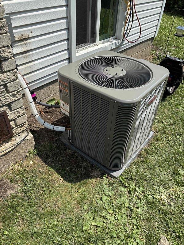 Completed installation of 2.5-ton air conditioning system at rear of residence. Positioned outdoor condensing unit on concrete pad adjacent to building foundation with proper clearances, connected refrigerant lines with insulation running through window opening to indoor components located in basement utility area. Verified all electrical connections, tested system operation, and confirmed proper refrigerant charge and airflow.