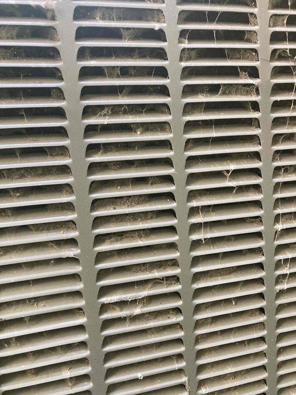 Responded to no cooling call on residential air conditioning system displaying red blinking fault indicator light. Upon inspection, found outdoor unit intake grille heavily obstructed with accumulated dust, lint, debris, and cobwebs restricting airflow to condenser coil. Cleaned and cleared ventilation grille to restore proper air circulation, documented conditions with photos, and system returned to normal operation after clearing blockage.