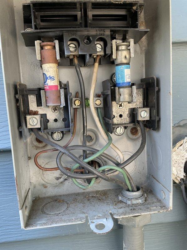 Responded to service call for non-operational AC fan. Upon arrival, inspected outdoor condensing unit electrical components and discovered severely corroded and aged disconnect box with deteriorated fuses and oxidized connections. Found left fuse holder contained worn cylindrical fuse showing significant corrosion on copper components, while right fuse holder had blue cylindrical fuse. Terminal block connections displayed weathering and oxidation consistent with extended outdoor exposure. Multiple wire connections with orange wire caps showed signs of age and environmental degradation. Replaced failed fuses, cleaned corroded terminals, and verified all electrical connections were secure. Tested unit operation and confirmed AC fan motor now functions properly. Recommended monitoring system performance and considering disconnect box replacement due to advanced corrosion of enclosure components.
