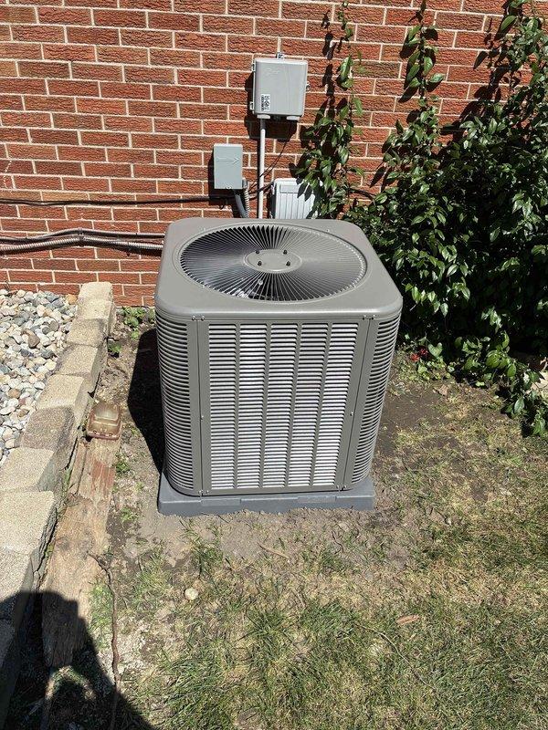 Completed installation of a 2.5-ton air conditioning system with matching evaporator coil at residential property. The outdoor condensing unit was positioned on a concrete pad in the rear yard with proper electrical connections established, including conduit and disconnect box mounted to exterior brick wall. System was charged with refrigerant, tested using digital manifold gauges, and verified operational with proper pressure and temperature readings across both high and low sides.