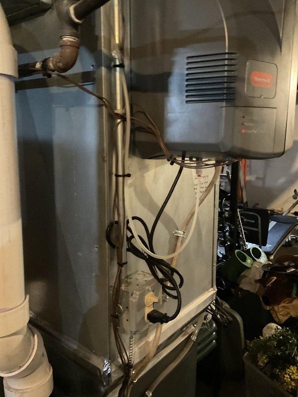 Conducted on-site evaluation of existing HVAC system for air conditioning replacement estimate. Inspected current air handler unit with metallic plenum assembly, verified condensate drain line configuration with white PVC piping, and assessed overall system condition in mechanical room. Evaluated existing basement utility equipment including water storage tank with copper connections and wall-mounted gray HVAC component with ventilation slots. Documented equipment specifications, spatial constraints, and installation requirements through detailed photographic documentation to provide accurate replacement system recommendations and sizing calculations for new air conditioning unit.