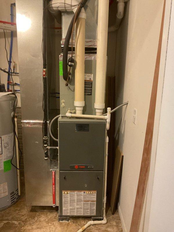 Responded to service call for damaged air conditioning system. Upon inspection of outdoor Trane condensing unit, confirmed that a cooking utensil had fallen into the equipment, causing compressor damage and complete refrigerant loss. Documented equipment condition with photographs showing the outdoor unit on concrete pad and associated indoor furnace system in basement utility area. Provided estimate for full AC system replacement due to extent of compressor damage and refrigerant leak.