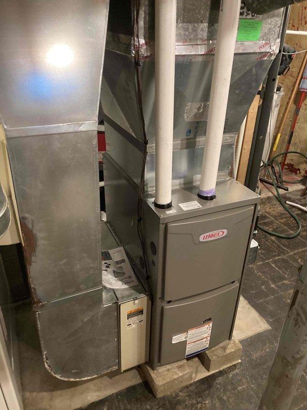 Completed mechanical installation of Lennox 70,000 BTU furnace system in basement utility area. Positioned unit on wooden blocking for proper elevation and leveling on concrete floor. Installed white PVC intake and exhaust venting through exterior brick wall, securing pipes with appropriate supports and terminations. Connected furnace to existing ductwork system using flexible duct connectors and sealed all joints. Verified all gas connections were properly reconnected and tested for leaks. System successfully commissioned and operational upon completion.