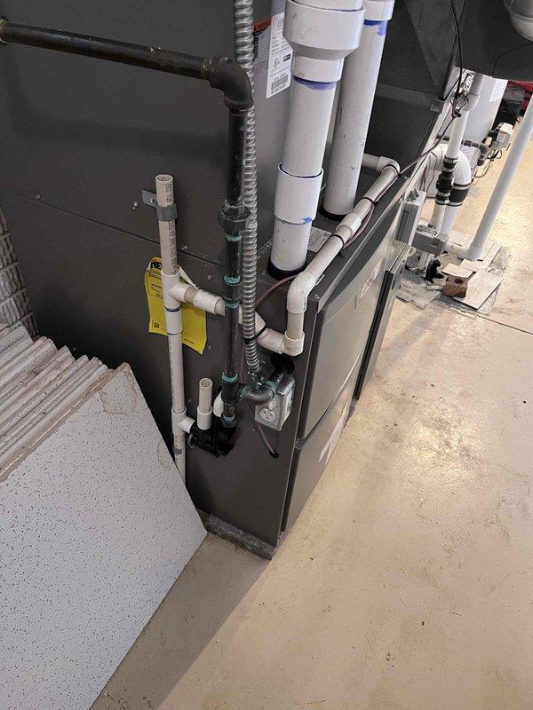 Completed installation of 110,000 BTU furnace with associated components in basement utility area. Installed new furnace unit on concrete pad with proper white PVC intake and exhaust venting system, including multiple diameter pipes with appropriate fittings and elbows for code-compliant ventilation. Ran gray flexible electrical conduit for power supply protection, installed humidifier unit, and set up new thermostat. All condensate drainage lines properly routed and secured with black fittings connecting PVC sections. System tested and verified operational upon completion.