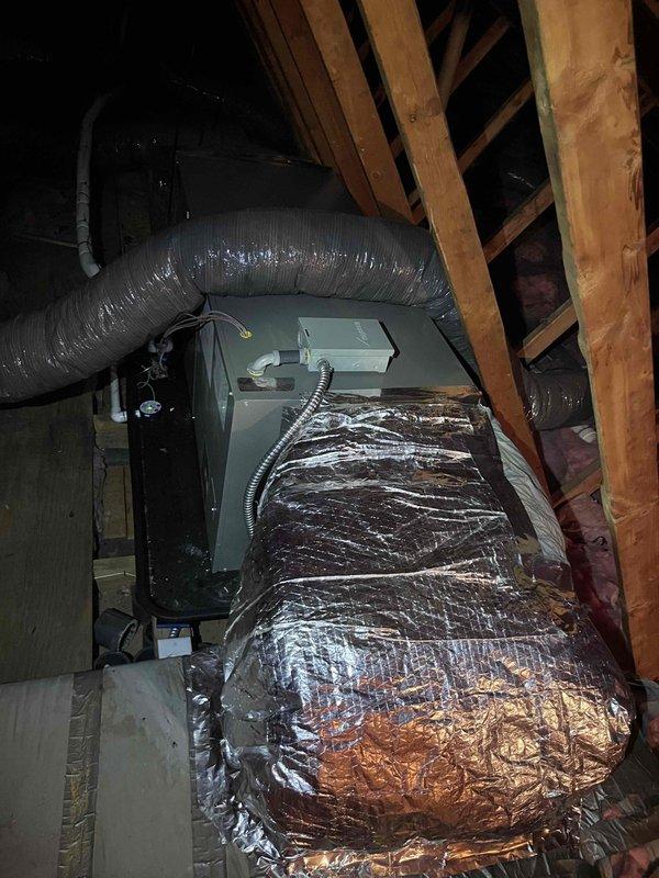 Completed final installation of HVAC air handler unit in attic space with associated ductwork and insulation. Installed exterior PVC condensate drain line along building exterior corner, running from attic through brick and siding sections to ground level. Verified proper air handler positioning, secured flexible ductwork connections, and ensured reflective insulated duct runs were properly sealed and supported. Confirmed condensate drain line was securely mounted with appropriate brackets and draining properly. System tested and operational upon completion of warranty work.