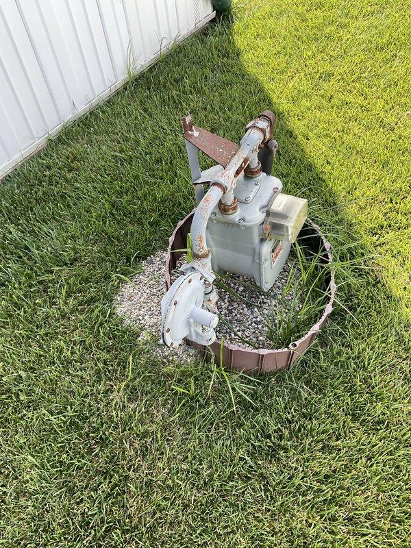 Performed comprehensive air conditioning replacement estimate for aging residential cooling system. Evaluated existing outdoor condensing unit showing significant deterioration with visible rust and corrosion on disconnect box, metal conduits, and mounting components. Unit confirmed to be approximately fifteen years old, exceeding typical service life expectancy. Inspected indoor programmable Ritetemp thermostat for compatibility assessment with potential replacement equipment. Documented current system configuration including outdoor unit placement on gravel pad with metal ring border adjacent to property structure, electrical disconnect condition, and refrigerant line routing. Photographed equipment conditions to support replacement recommendations. Customer requesting complete system replacement proposal.