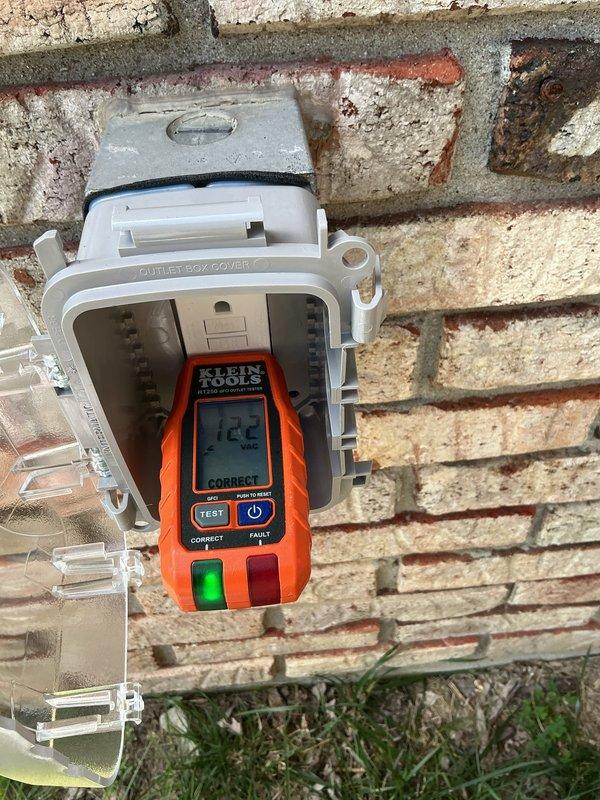Installed GFCI outlet in exterior weatherproof box mounted on brick wall foundation. Tested installed receptacle using Klein Tools electrical tester, which confirmed proper voltage reading of 122V and verified correct GFCI functionality and ground protection.