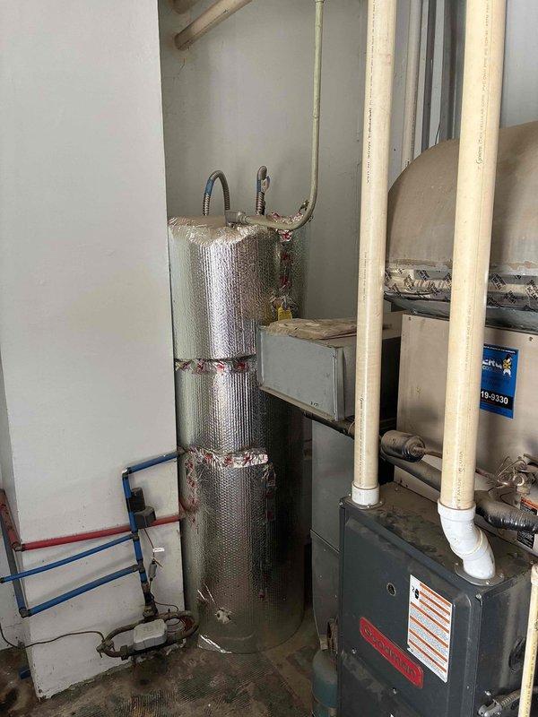 Conducted on-site estimate for replacement of existing Goodman furnace system in residential basement mechanical room. Evaluated current HVAC configuration including furnace, ductwork plenum assembly, and adjacent water heater placement in confined utility space. Documented equipment condition through photographs showing gray metal furnace unit with vertical duct transitions, PVC venting, and flexible ductwork connections. Assessed mechanical room layout with exposed framing and concrete flooring to determine replacement equipment specifications and installation requirements. Homeowner present during evaluation to discuss system replacement options and answer questions regarding existing older unit performance.