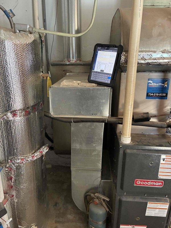 Conducted on-site estimate for replacement of existing Goodman furnace system in residential basement mechanical room. Evaluated current HVAC configuration including furnace, ductwork plenum assembly, and adjacent water heater placement in confined utility space. Documented equipment condition through photographs showing gray metal furnace unit with vertical duct transitions, PVC venting, and flexible ductwork connections. Assessed mechanical room layout with exposed framing and concrete flooring to determine replacement equipment specifications and installation requirements. Homeowner present during evaluation to discuss system replacement options and answer questions regarding existing older unit performance.