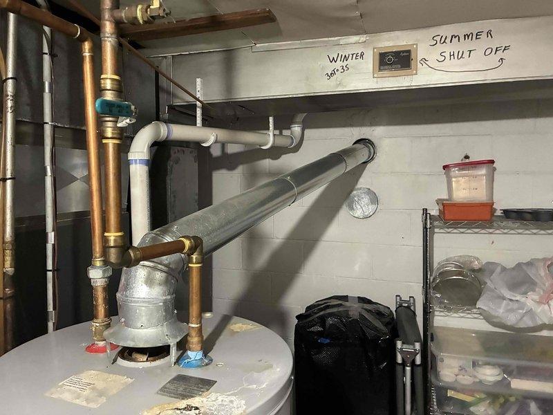 Conducted on-site assessment of non-functioning A.O. Smith standard natural draft water heater located in basement utility area. Evaluated existing unit configuration including copper supply piping, flue venting system, pressure relief valve assembly, and electrical connections. Documented current installation conditions and measured available space for replacement unit, noting concrete block wall construction and existing plumbing layout with PVC and copper pipe runs.
