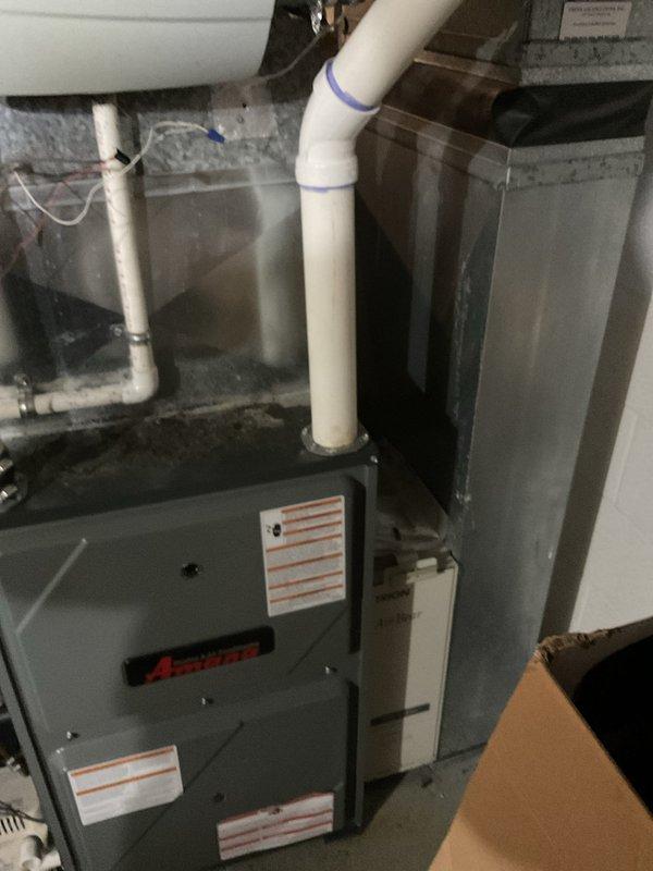 Conducted comprehensive estimate for complete HVAC system replacement of 10-12 year old equipment currently operational but nearing end of service life. Evaluated existing furnace installation in basement utility area with vertical PVC venting system and associated drainage piping, as well as outdoor condensing unit positioned on concrete pad with river rock landscaping and electrical service connections via wall-mounted meter and conduit system.