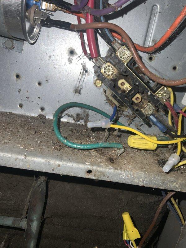 # HVAC Service Report - No Cool Condition

Responded to service call for air conditioning system not cooling on unit over 10 years old. Upon arrival, performed visual inspection of outdoor condensing unit and electrical components. Found outdoor disconnect box mounted on exterior brick wall showing extensive weathering, rust, and corrosion throughout interior components. Circuit breaker and contactor housing displayed significant deterioration with rust stains streaking from connection points and exposed bare metal where paint had chipped away.

Opened equipment panels to inspect internal electrical connections and components. Located contactor assembly with brass terminal block showing signs of age and wear. Examined all wire connections including power supply wires and control circuit wiring. Found accumulated dirt, grime, and debris throughout equipment interior affecting multiple components. Metal surfaces displayed considerable discoloration and staining consistent with age and en