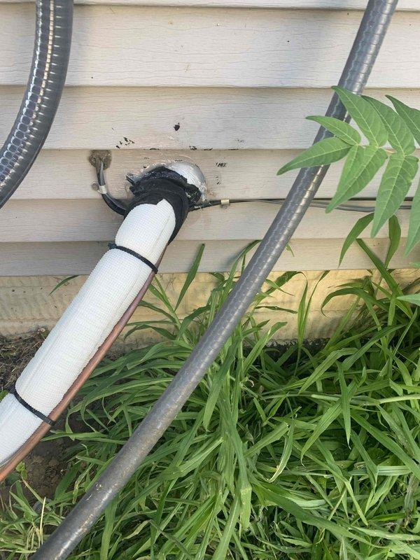 Responded to callback for HVAC installation to address exterior penetration sealing. Removed deteriorated thumb gum sealant from white PVC condensate drain line where it exits through building siding. Cleaned penetration area and surrounding discolored siding material. Applied silicone sealant around pipe penetration to ensure proper weatherproofing and prevent water intrusion. Verified all mounting straps secure and condensate line properly supported. Documented completed work with photographs showing corrected penetration seal and exterior utility connections.