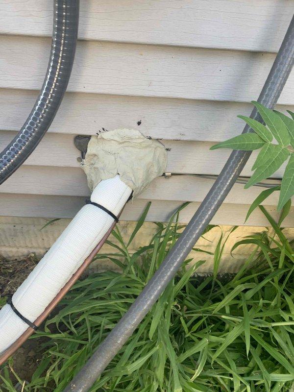 Responded to callback for HVAC installation to address exterior penetration sealing. Removed deteriorated thumb gum sealant from white PVC condensate drain line where it exits through building siding. Cleaned penetration area and surrounding discolored siding material. Applied silicone sealant around pipe penetration to ensure proper weatherproofing and prevent water intrusion. Verified all mounting straps secure and condensate line properly supported. Documented completed work with photographs showing corrected penetration seal and exterior utility connections.