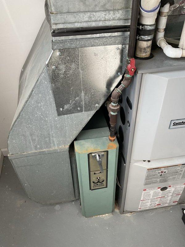 Conducted on-site assessment of existing residential HVAC system for replacement estimate. Inspected Comfortmaker furnace/air handler unit in basement utility area, evaluating overall condition of equipment, ductwork, and associated components. Documented aging galvanized metal ductwork showing dust accumulation and discoloration, existing white cabinet furnace with digital control panel, and auxiliary equipment including light blue-green condensate basin. Examined plumbing connections including PVC vent piping, copper lines, and shut-off valves for integration with new equipment installation. Photographed current system configuration, noting concrete block wall damage near equipment area that may require attention during replacement. Provided comprehensive equipment replacement recommendations based on existing infrastructure and spatial constraints.