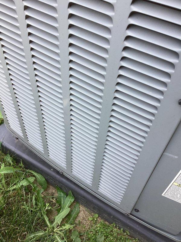 # AC NOT WORKING 12-489

Responded to no cooling call on outdoor condensing unit. Upon arrival, performed visual inspection of exterior HVAC equipment. Unit appeared to be 10+ years old based on condition and weathering patterns. Exterior casing showed normal aging consistent with outdoor installation, with louvers intact and properly aligned.

Documented equipment condition through photographs for service records. Unit positioned on ground-level pad with adequate clearance for airflow. Ventilation grilles and horizontal louvers clean and unobstructed, allowing proper air circulation to internal components. No visible signs of physical damage, severe corrosion, or structural compromise to cabinet or protective casing.

Noted manufacturer identification label present on unit exterior for reference. Surrounding area showed vegetation growth near base, which could potentially restrict airflow if left unmanaged. Black protective base trim intact and properly seated against mounting surface