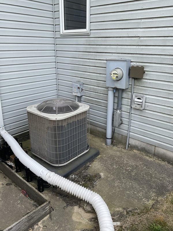 Conducted on-site evaluation of residential central air conditioning system at end of service life. Assessed exterior condensing unit positioned on concrete pad adjacent to building exterior, documenting equipment condition, installation configuration, and surrounding utility connections including electrical meter and disconnect. Photographed unit placement, clearances, and existing electrical infrastructure to support replacement system specifications and installation planning.