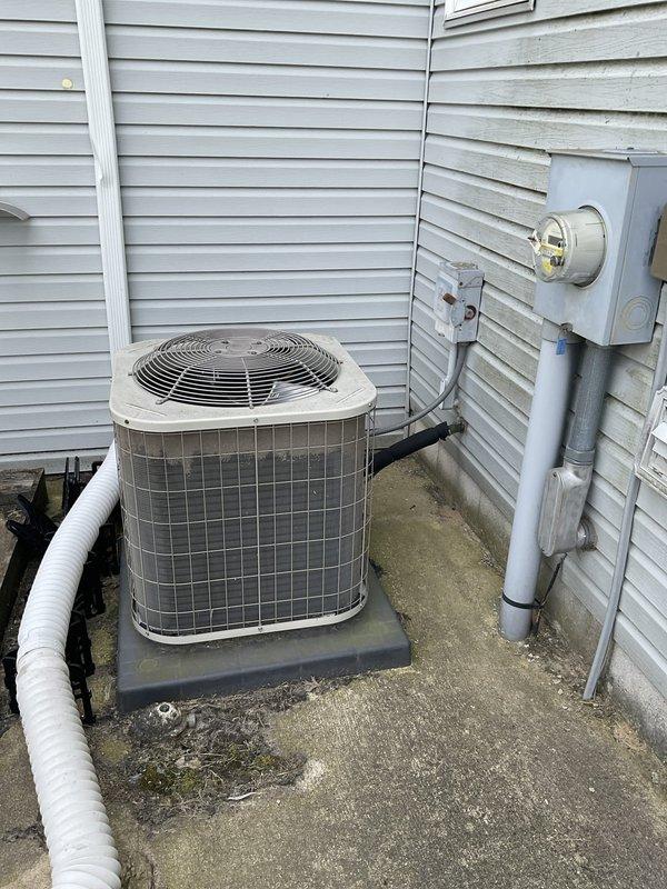 Conducted on-site evaluation of residential central air conditioning system at end of service life. Assessed exterior condensing unit positioned on concrete pad adjacent to building exterior, documenting equipment condition, installation configuration, and surrounding utility connections including electrical meter and disconnect. Photographed unit placement, clearances, and existing electrical infrastructure to support replacement system specifications and installation planning.