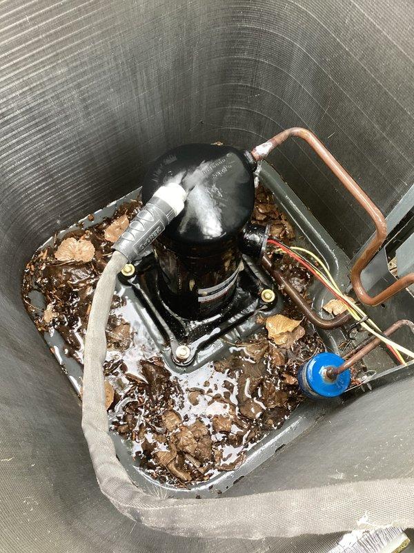 # HVAC Service Report - No Cool Condition

Responded to emergency service call for air conditioning system not cooling adequately with rising indoor temperatures. Upon arrival, performed visual inspection of outdoor condensing unit and found significant debris accumulation around compressor base, including leaves, dirt, and standing water creating obstruction to proper airflow and drainage.

Conducted electrical diagnostics using clamp meter to measure amperage draw on compressor circuit. Recorded readings to verify compressor operation and compare against manufacturer specifications. Inspected refrigerant lines, electrical connections, and capacitor for proper function and signs of wear.

Identified debris buildup as contributing factor to reduced cooling efficiency. Removed accumulated organic matter and standing water from compressor housing base to restore proper drainage and prevent future corrosion. Cleaned area around compressor to eliminate airflow restrictions.

Verified all e