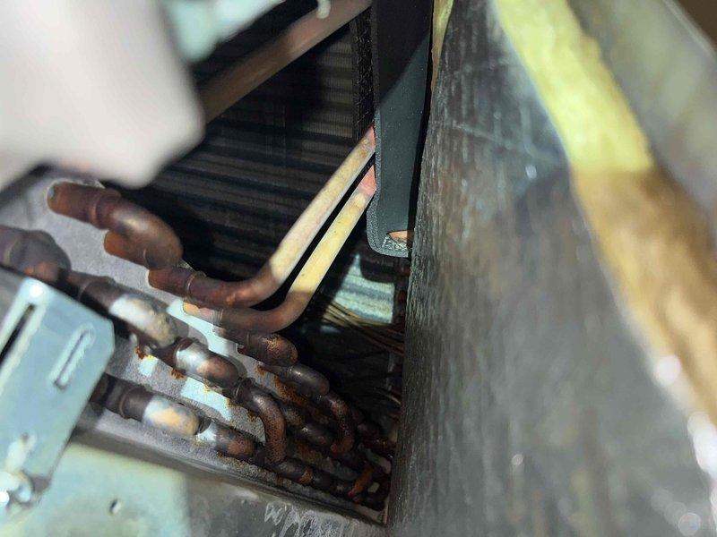 Completed preventive maintenance inspection under Club AC12-4 agreement. Performed comprehensive system evaluation including inspection of indoor evaporator coil assembly and refrigerant line sets. Documentation revealed significant rust and corrosion present on copper refrigerant lines, indicating extended service life or moisture exposure concerns. Photographed deteriorated piping conditions showing brown oxidation and surface rust on tubing connections to air handling components. Inspected finned coil heat exchanger and associated electrical junction boxes. System operational at time of service visit with noted concerns regarding refrigerant line integrity for future monitoring.