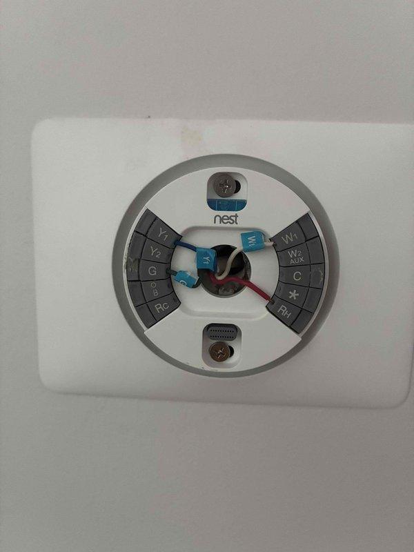 Conducted estimate for R22 refrigerant system with reported flat/no cooling condition. Inspected Nest thermostat installation and wiring configuration, documenting terminal connections including Y1, Y2, G, RC, W1/E, W2/AUX, and C terminals with multiple blue wires and red wire properly connected. Evaluated basement mechanical area with exposed HVAC ductwork and electrical infrastructure to assess system accessibility and replacement requirements for aging R22 equipment.