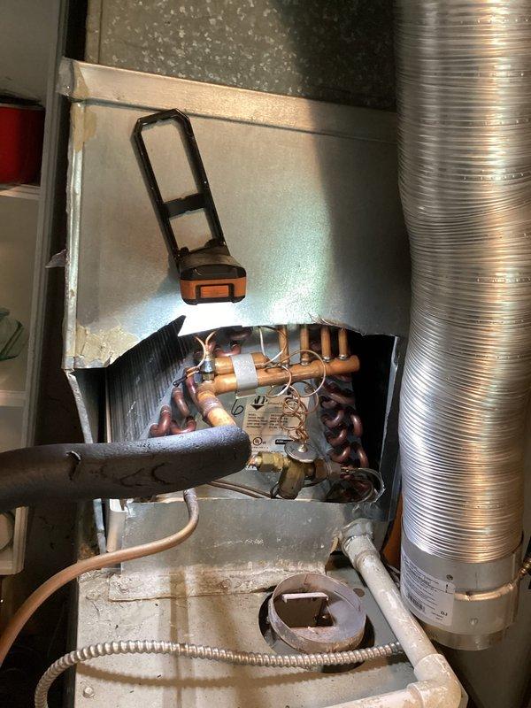 # HVAC Service Completed

Responded to no-cooling complaint with system blowing air but compressor not operating. Performed diagnostic inspection of split system air conditioning unit. Removed access panel and examined evaporator coil assembly and refrigerant circuit components. Inspected copper refrigerant lines, evaporator coil condition, and associated mechanical components within air handler cabinet. Documented internal system condition including coil assembly, condensate drain pan with visible staining indicating normal operation history, and flexible ductwork connections. Photographed refrigerant circuit components including coils, copper piping, and what appears to be a filter drier or service valve assembly with manufacturer specifications visible. System age could not be confirmed from available information during inspection.