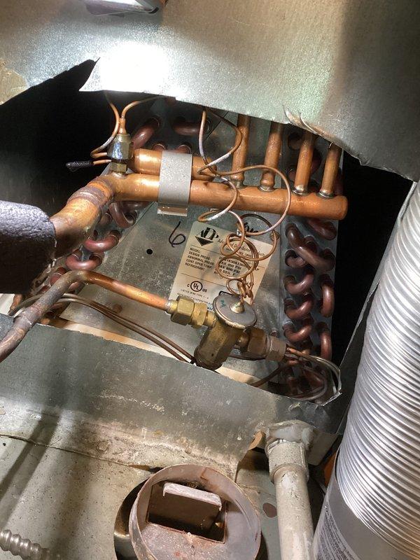 # HVAC Service Completed

Responded to no-cooling complaint with system blowing air but compressor not operating. Performed diagnostic inspection of split system air conditioning unit. Removed access panel and examined evaporator coil assembly and refrigerant circuit components. Inspected copper refrigerant lines, evaporator coil condition, and associated mechanical components within air handler cabinet. Documented internal system condition including coil assembly, condensate drain pan with visible staining indicating normal operation history, and flexible ductwork connections. Photographed refrigerant circuit components including coils, copper piping, and what appears to be a filter drier or service valve assembly with manufacturer specifications visible. System age could not be confirmed from available information during inspection.