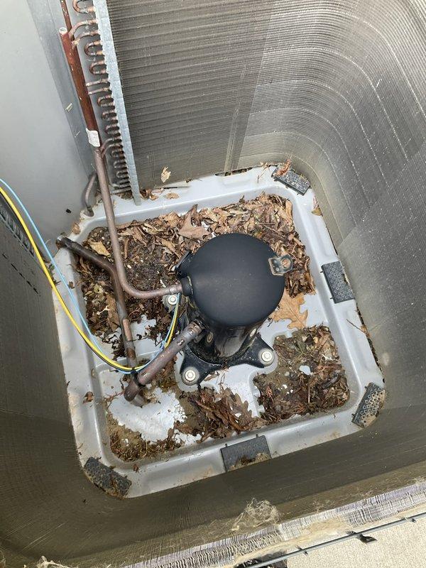 # HVAC Maintenance - Agreement Visit AC&SI

Completed comprehensive annual air conditioning tune-up and preventive maintenance on outdoor condensing unit per prepaid maintenance agreement. Unit is an older model AC system with black protective cage enclosure, positioned on concrete pad with gravel landscaping beside residence.

## Work Performed

Upon arrival, conducted visual inspection of outdoor condenser unit. Noted significant accumulation of leaves, twigs, and organic debris in base drain pan and around internal components. Debris had decomposed over time, creating potential drainage issues and restricting airflow around compressor assembly.

Removed protective cage to access internal components. Cleared all leaves and organic material from white plastic drain pan at base of unit. Removed debris from around black cylindrical compressor unit and mounting brackets. Cleaned accumulated dirt and vegetation from area surrounding copper refrigerant lines.

Inspected condenser coil and 