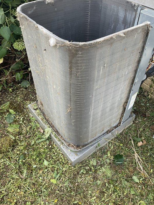 Completed scheduled CLUB AC 10-2 maintenance agreement visit on outdoor air conditioning condenser unit. Unit exhibited heavy accumulation of dirt, debris, and organic matter throughout interior surfaces and exterior coil fins, indicating extended period without maintenance. Performed thorough cleaning and inspection of condenser coil, removed significant buildup of dust, soil, and decomposed plant material from interior components and metal surfaces. Cleared vegetation growth from around unit base and perimeter to ensure proper airflow and drainage. Documented pre-service condition showing weathering, grime, discoloration, and environmental buildup on metallic surfaces and fins. System operational following completion of maintenance procedures.