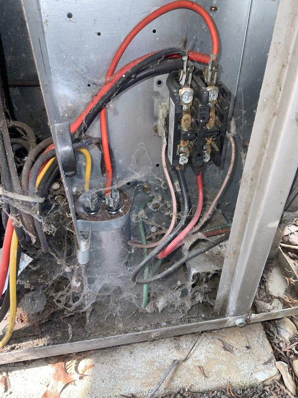 Responded to no-cool complaint with air conditioning system blowing warm air throughout the residence. Upon inspection, found outdoor condensing unit with significant accumulation of dirt, debris, and organic material in cabinet and on internal components, including capacitor and contactor assembly. Examined electrical connections and control panel wiring, noting system showed signs of age and environmental exposure with visible weathering on metal surfaces. Documented condition of unit interior, electrical components, and control board with multiple wire connections. Unit components including cylindrical capacitor and black contactor relay were assessed for proper operation and connection integrity.