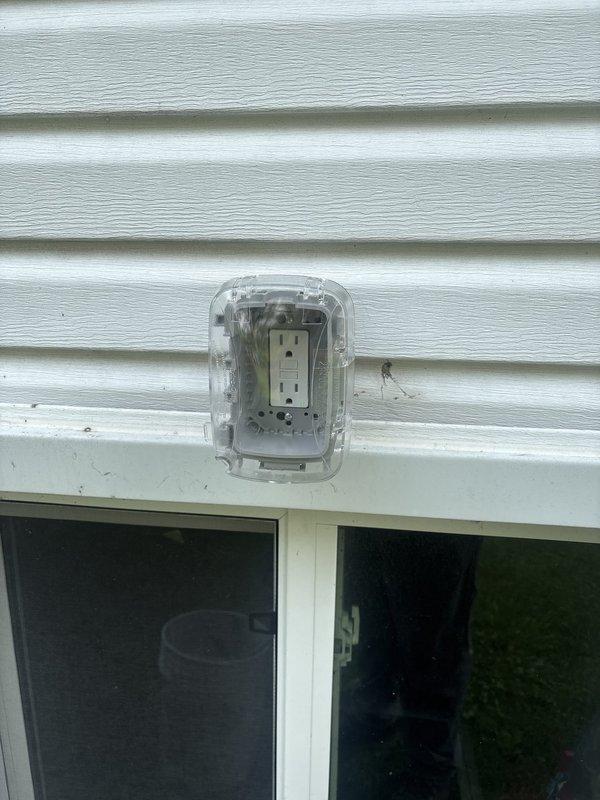 Installed GFCI-protected outdoor electrical outlet with weatherproof bubble cover on exterior wall with vinyl siding. Additionally installed exterior wall-mounted light fixture with transparent protective cover and weather-resistant housing to provide adequate outdoor illumination. Both installations completed to code specifications for outdoor electrical applications.