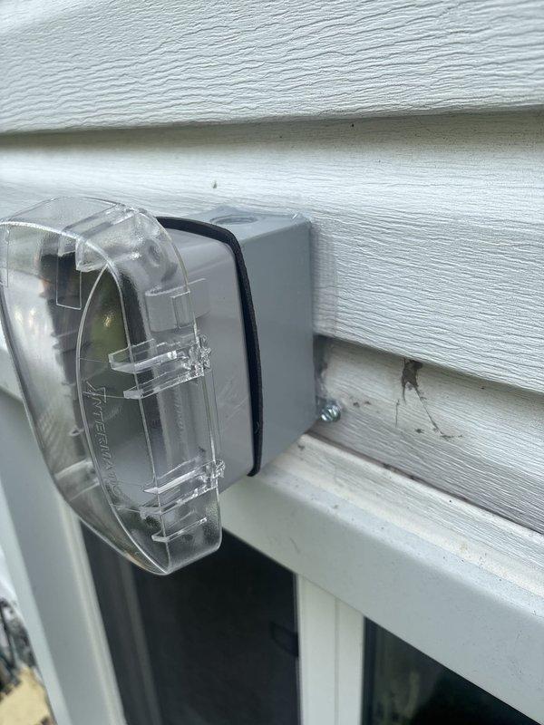Installed GFCI-protected outdoor electrical outlet with weatherproof bubble cover on exterior wall with vinyl siding. Additionally installed exterior wall-mounted light fixture with transparent protective cover and weather-resistant housing to provide adequate outdoor illumination. Both installations completed to code specifications for outdoor electrical applications.