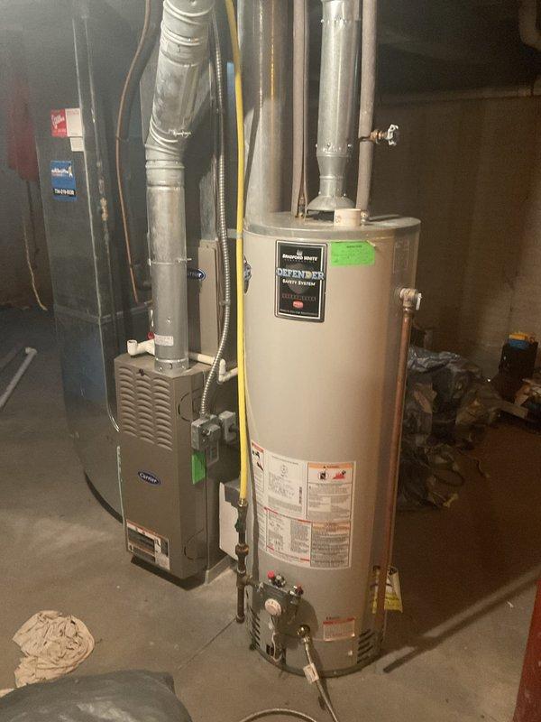 Conducted comprehensive estimate visit for HVAC system replacement, water heater replacement, and air conditioning unit in residential basement utility area. Assessed existing furnace with intake grille, cylindrical water heater with flue pipe and copper connections, and ductwork system including vertical metal duct runs and junction box installations. Documented current equipment conditions and specifications through detailed photography for preparation of replacement quotes covering all three components.