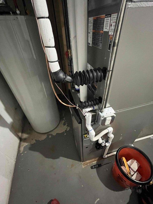 # HVAC Maintenance Agreement Visit - Air Conditioner Tune-Up Completed

Performed comprehensive preventive maintenance on residential air conditioning system as part of prepaid maintenance agreement. No operational issues or concerns reported prior to service visit.

## Work Performed

Conducted complete air conditioner tune-up and inspection on indoor air handler unit located in basement mechanical room. Performed visual inspection of all accessible components including refrigerant line insulation, electrical connections, and condensate drainage system. Verified proper installation of vibration dampeners and flexible connectors on refrigerant lines. Inspected copper refrigerant piping with white insulation wrap secured with mounting straps for any signs of damage or deterioration.

Examined manufacturer information plate and verified system specifications. Assessed condition of PVC condensate drain lines and fittings for proper drainage and potential blockages. Checked air handler cab