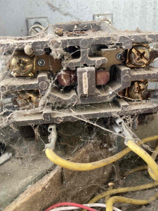 Responded to no cooling complaint on residential air conditioning system. Upon arrival, found unit running but not cooling the home. Performed diagnostic testing and discovered failed contactor with severe corrosion and deterioration preventing proper compressor operation. Contactor showed heavy buildup of dirt, dust, and oxidation affecting electrical connections. Used multimeter to verify 0 volts at contactor, confirming complete electrical failure. Inspected terminal block connections and found extensive cobweb accumulation and aged wiring with signs of neglect. Replaced defective contactor and cleaned electrical connections at terminal block. Removed debris and cobwebs from electrical components. Tested system operation after repairs and verified proper voltage delivery to compressor. Unit now cooling properly with all electrical connections secure and functioning as designed.