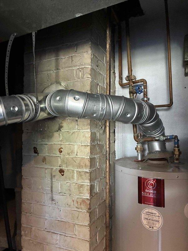 Responded to emergency service call for non-functional tanked water heater replacement in residential basement utility room. Assessed existing white cylindrical water heater unit with power vent configuration installed against painted cinder block wall on concrete floor. Provided comprehensive estimate for complete water heater replacement including removal of failed unit, installation of new tanked water heater with proper venting through existing flexible metallic duct system, connection to existing copper supply lines with blue-handled shutoff valves, and compliance with current plumbing codes for basement installations.