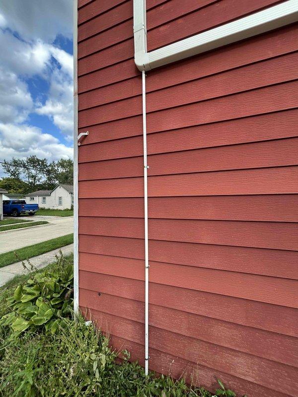 Completed final installation of mini split system on residential property with red lap siding. Mounted outdoor condenser unit on exterior wall with proper clearances and drainage, secured all refrigerant line sets and electrical connections, and verified system operation. Installation includes white PVC line set cover for clean exterior appearance and protection of refrigerant lines.