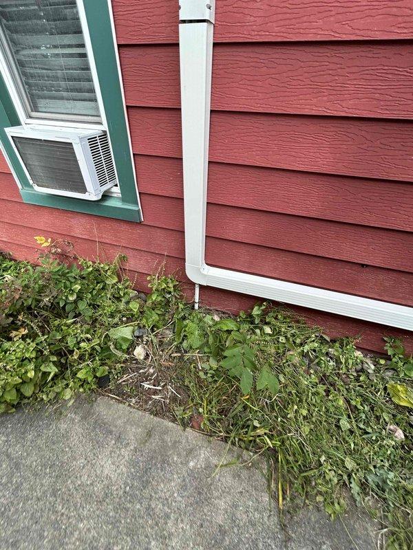 Completed final installation of mini split system on residential property with red lap siding. Mounted outdoor condenser unit on exterior wall with proper clearances and drainage, secured all refrigerant line sets and electrical connections, and verified system operation. Installation includes white PVC line set cover for clean exterior appearance and protection of refrigerant lines.
