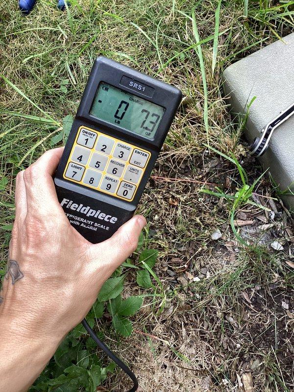 Completed Club AC10-2 preventive maintenance agreement visit for air conditioning and system inspection. Inspected exterior refrigerant line connections and service valves, noting aged brass fittings with weathering and patina consistent with outdoor installation. Verified refrigerant charge using calibrated digital scale, obtaining system weight measurement to confirm proper charge levels and system performance parameters are within manufacturer specifications.