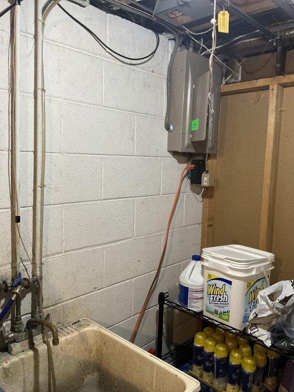 Conducted comprehensive site assessment for complete HVAC system replacement at residential property. Evaluated existing outdoor condensing unit positioned on concrete pad against brick exterior, noting cylindrical configuration with vertical cooling fins and top-mounted fan assembly. Inspected electrical disconnect box and conduit connections serving outdoor equipment. Assessed indoor basement infrastructure including electrical panel, existing ductwork, and utility area layout to determine installation requirements for new furnace and air handler. Documented current system configuration and measured available space for equipment replacement. Photographed existing equipment conditions and electrical service to support replacement proposal specifications.