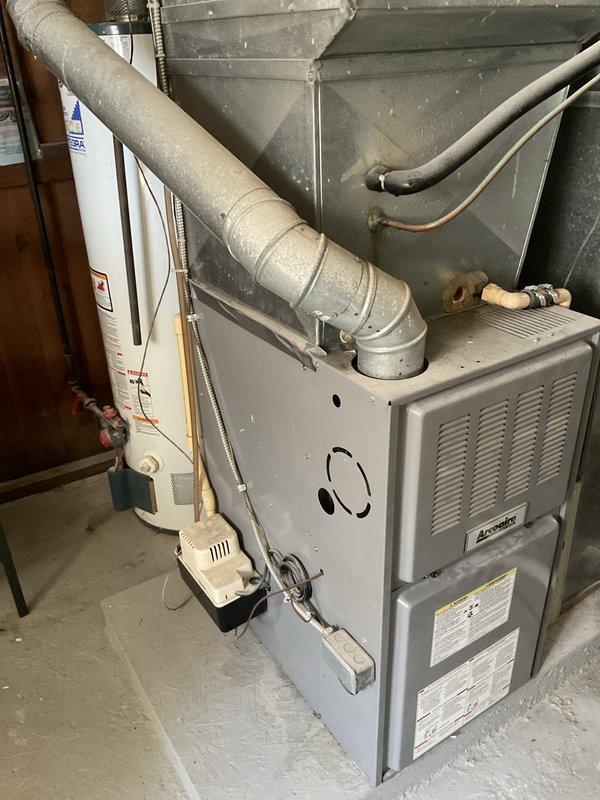 Provided estimate for complete HVAC system replacement including furnace and air conditioning unit. Current system is non-operational with unknown equipment age. Existing installation consists of basement-located gas furnace with associated ductwork, condensate pump, and outdoor condenser unit positioned in below-grade window well with PVC drain line and refrigerant lines running through exterior wall.