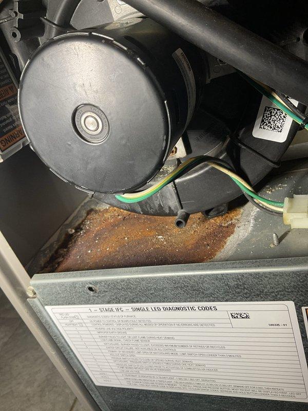 Completed preventive maintenance agreement visit on air conditioning and split system. Upon inspection, found significant rust corrosion and mineral deposit buildup in the drain pan beneath the blower motor assembly, indicating ongoing moisture accumulation and potential drainage issues. Documented condition of internal components including blower motor, electrical connections, and grounding wires. All mechanical and electrical components were inspected and found operational. System exterior and access panels were examined and photographed for maintenance records.