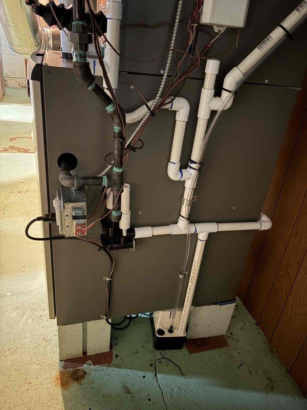 Completed full HVAC system installation including a 70,000 BTU furnace, 2-ton air conditioning system, boiler, and humidifier. Installed gray cabinet-style air handler unit in basement utility area with proper mounting and positioning. Ran and secured white PVC drainage lines from unit along floor and to ceiling using appropriate clips and connectors. Completed all electrical connections including flexible metallic conduit, junction box installation, and control panel wiring. Configured proper drainage system integration with existing sump pump pit. Verified all mechanical systems operational and reconnected electrical components per specifications.